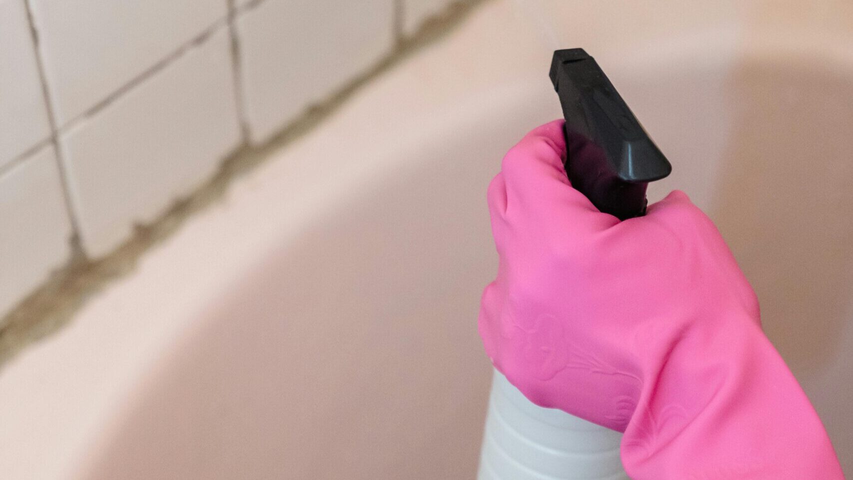 욕실에 타일 곰팡이를 세정제 스프레이로 청소하는 고무장갑 착용한 손